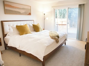 Un dormitorio con una cama grande, ropa de cama blanca y vistas al exterior a través de una puerta corrediza de vidrio.