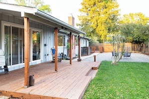 Una terraza de madera con un patio cubierto, un jardín cercado y un árbol pequeño.