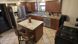 A kitchen with a central island, stainless steel appliances, wooden cabinets, and a tiled floor. - Downtown, Old Town, Sawmill, 2-bedroom home in ABQ, additional parking available (Albuquerque)