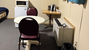 A small room with a round table, a microwave, a coffee maker, a trash bin, and a blue curtain. - Alliance valley Inn motel (Alliance)
