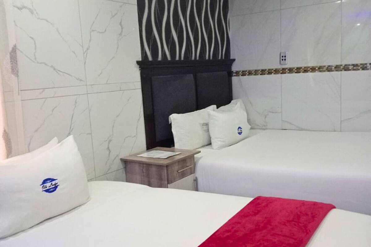 Una habitación de hotel con dos camas, una mesita de noche, una manta roja y un panel decorativo en la pared.
