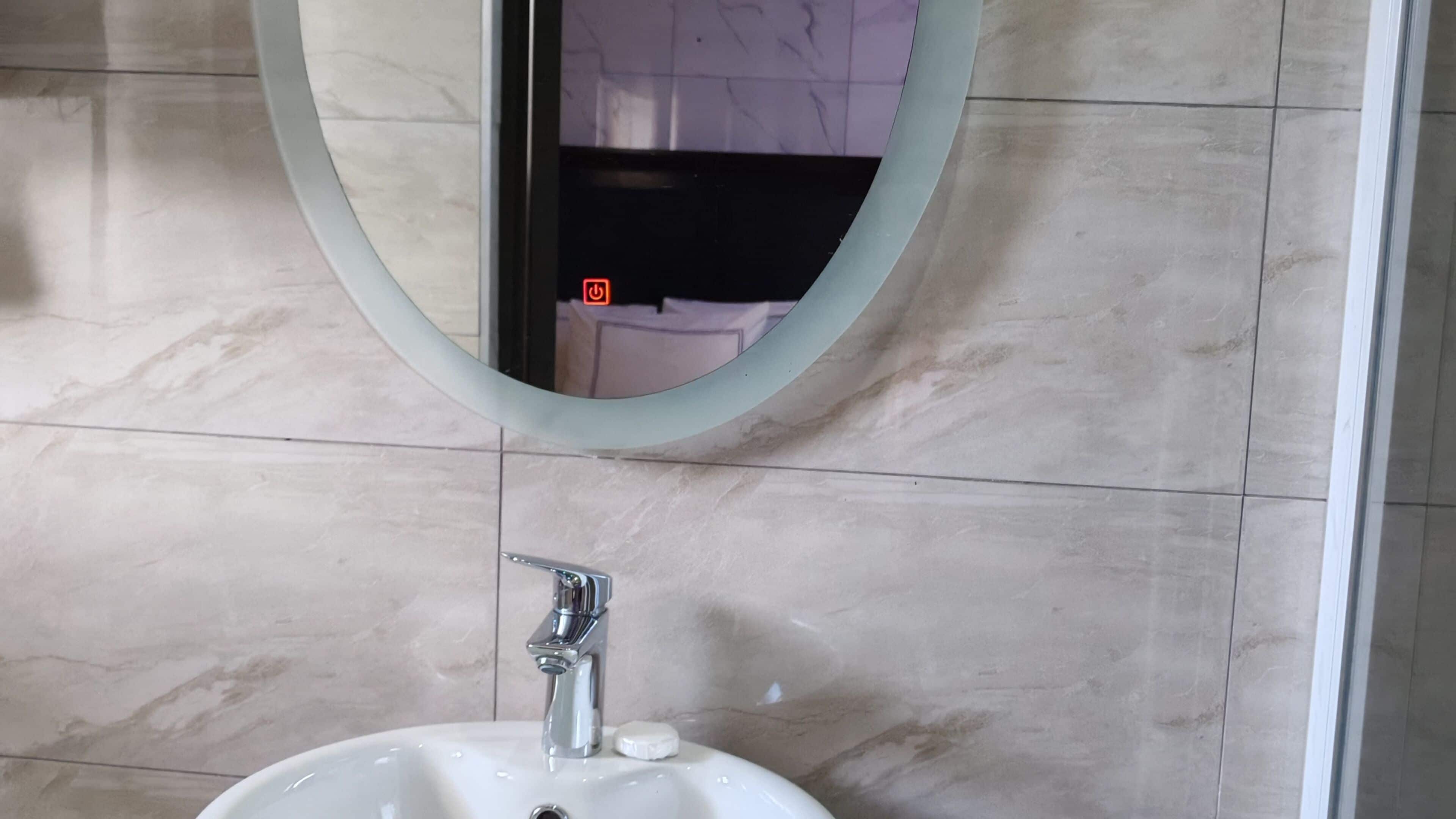 A bathroom with a white sink, a mirror, and a wall with a tiled pattern.