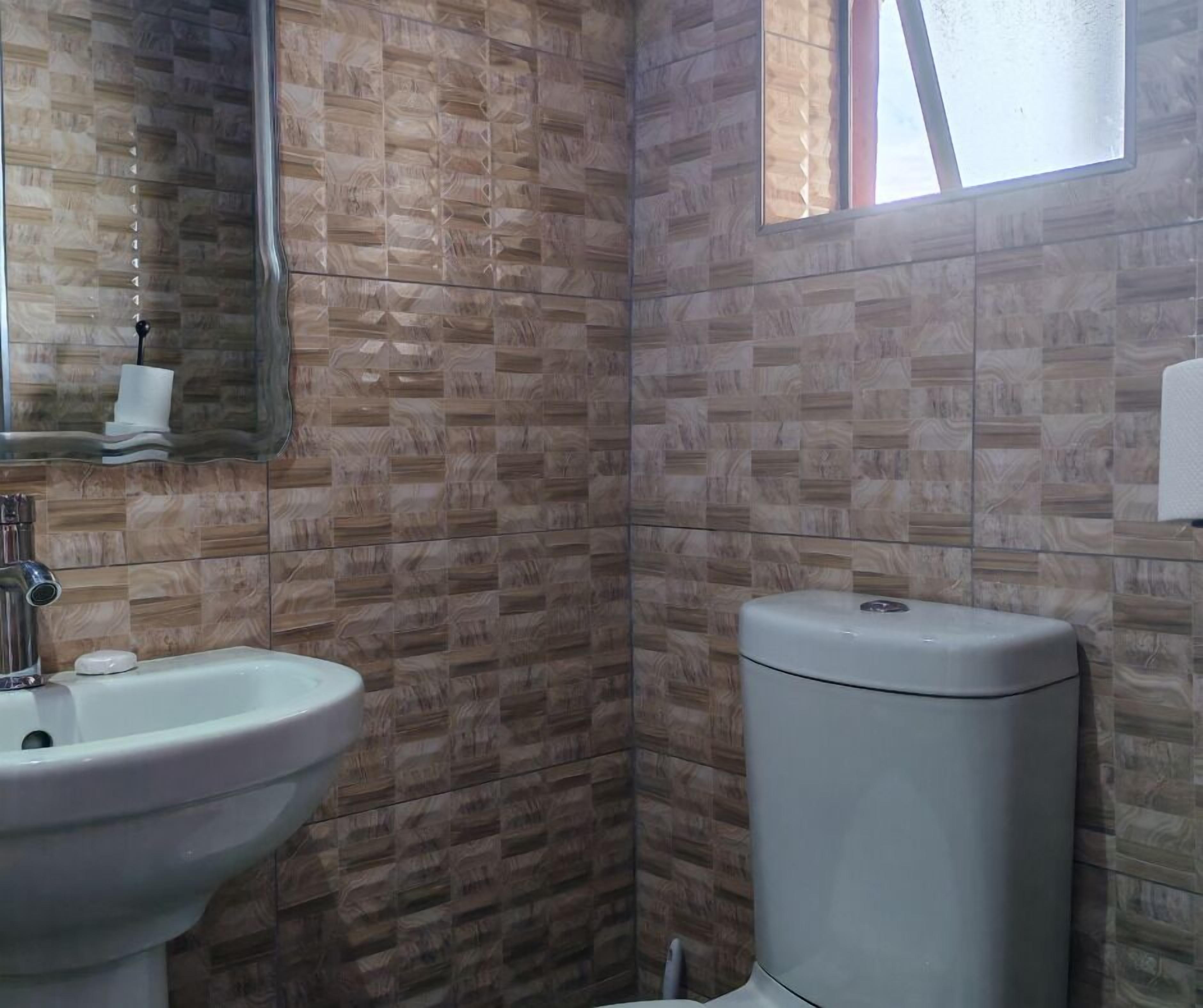 Une salle de bain avec un lavabo, un miroir et des toilettes, le tout adossé à un mur à motifs.