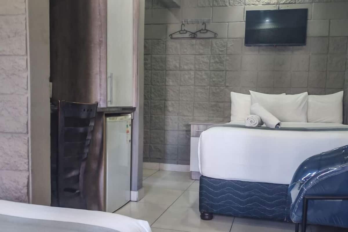Una habitación de hotel con una cama, un refrigerador pequeño, un televisor montado en la pared y piso de baldosas.