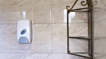 Un dispensador de gel antibacterial sujeto a una pared de azulejos junto a un marco de puerta de vidrio.