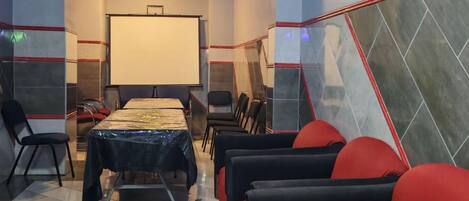 A conference room with a large table, chairs, a projector screen, and a tiled floor.