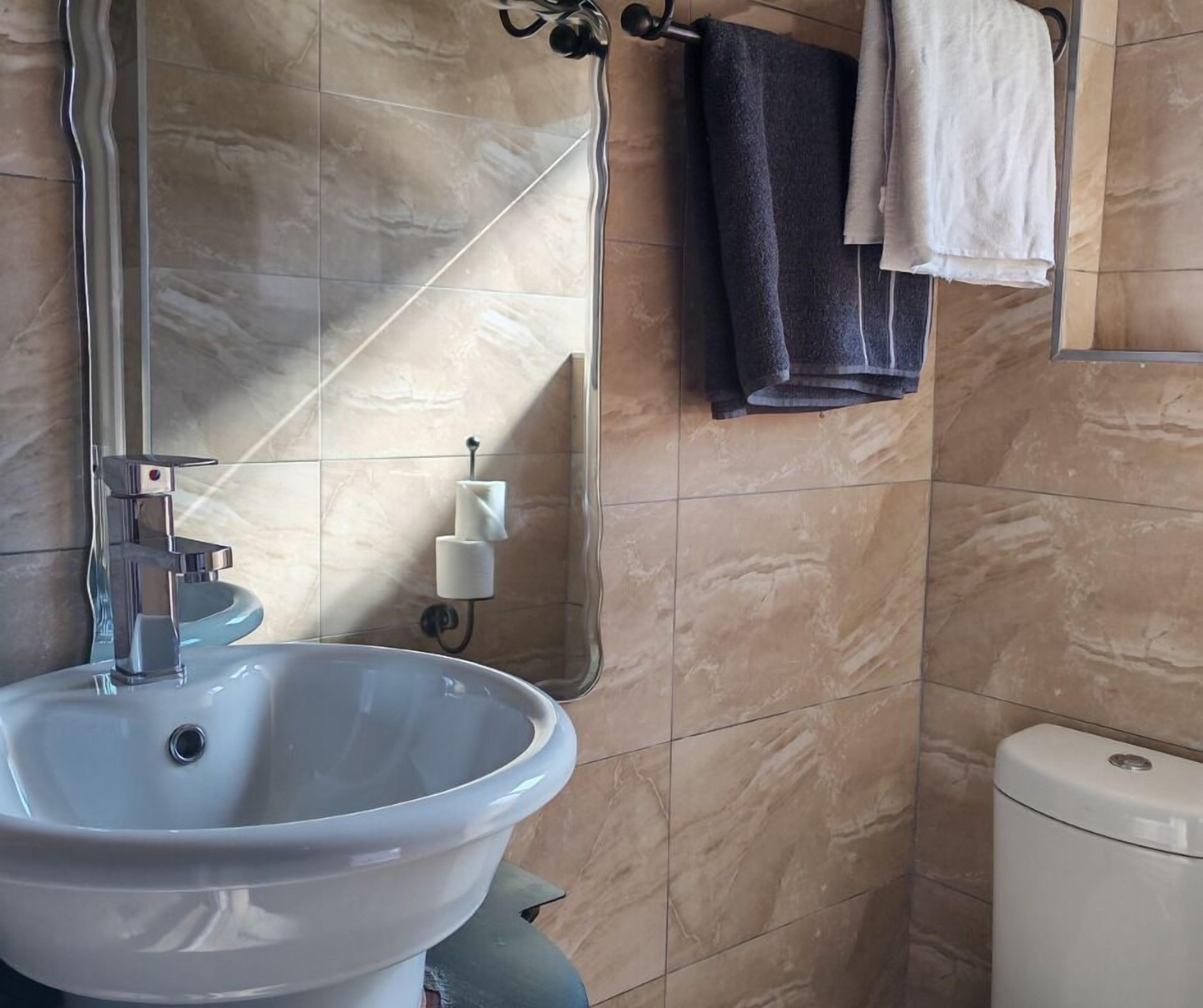 Une salle de bain avec un lavabo blanc, un miroir, un porte-serviettes avec des serviettes et des toilettes.