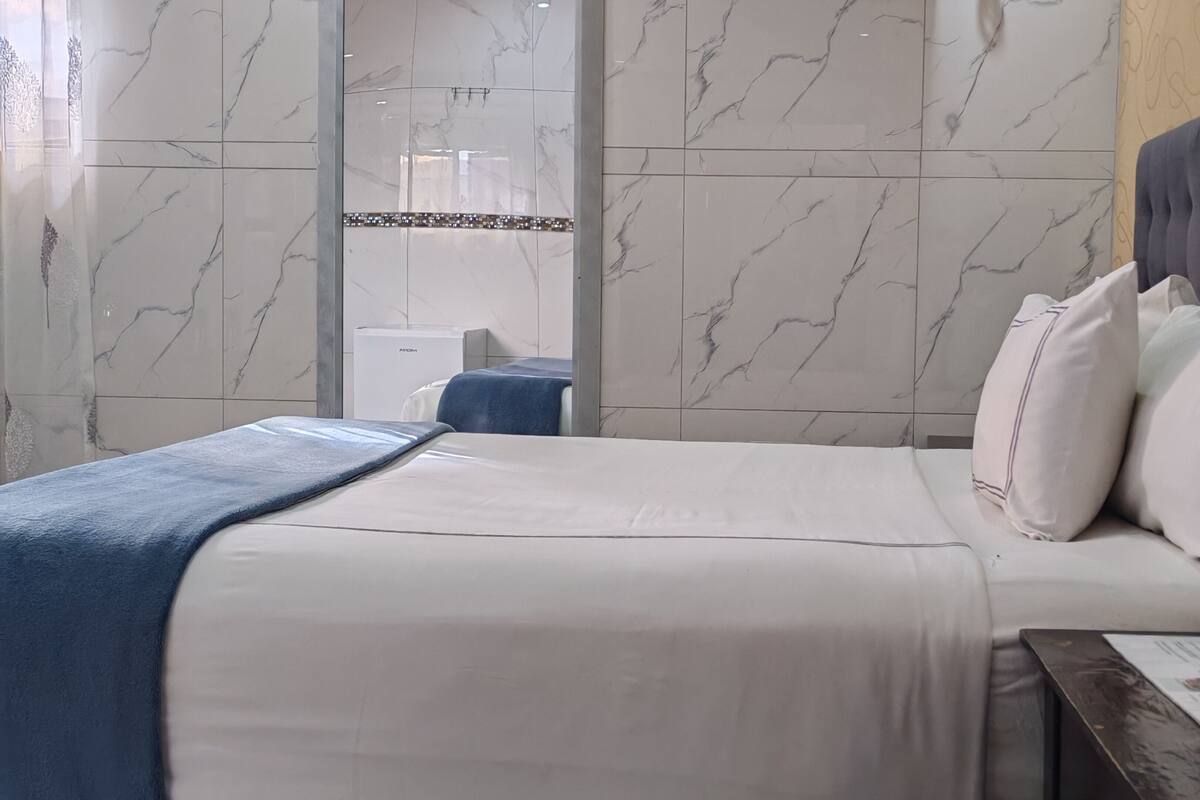 Una habitación de hotel con una cama, una mesita de noche, un espejo y una pared con estampado de mármol.