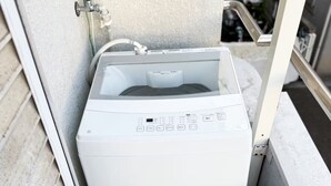 A compact, white portable washing machine in a narrow space with a textured wall and a metal railing. - （橘苑）Welcome to Orenyuan! A cozy Totoro-themed guesthouse in Osaka, (Osaka)