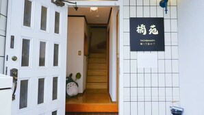 A hotel entrance with a white door, a signboard, a staircase, and a trash bin. - （橘苑）Welcome to Orenyuan! A cozy Totoro-themed guesthouse in Osaka, (Osaka)