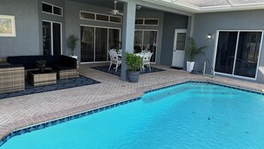 A modern outdoor pool area with a covered patio, seating, and a clear view of the pool. - Beautiful 3-bedroom Vacation Home located in beautiful Brooksville Fl (Spring Hill)