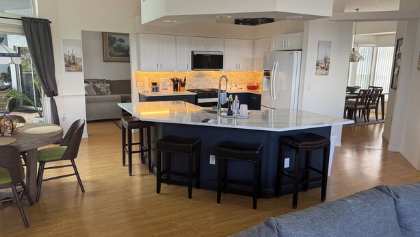 A modern kitchen with a central island, white cabinets, and a dining area with a gray sofa and wooden table. - Beautiful 3-bedroom Vacation Home located in beautiful Brooksville Fl (Spring Hill)