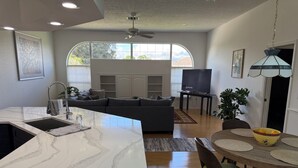 A modern kitchen with a large island, a dining area with a round table, and a living room with a sofa and TV. - Beautiful 3-bedroom Vacation Home located in beautiful Brooksville Fl (Spring Hill)
