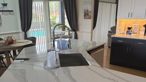A modern kitchen with a large island, dark cabinets, and a view of the outdoors. - Beautiful 3-bedroom Vacation Home located in beautiful Brooksville Fl (Spring Hill)