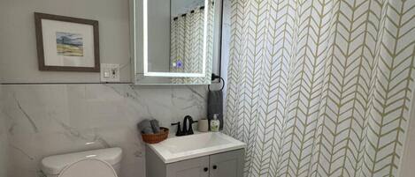 A bathroom with a toilet, sink, mirror, and shower curtain.