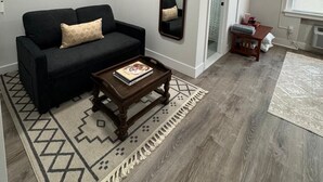 A modern living room with a black sofa, a wooden coffee table, a patterned rug, a large mirror, and a television.