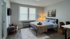 A compact bedroom with a bed, bedside table, lamp, and a painting on the wall.
