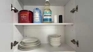 A kitchen with white cabinets, a coffee machine, sugar and coffee boxes, a dish soap bottle, a dish brush, and a Wesson vegetable oil bottle.
