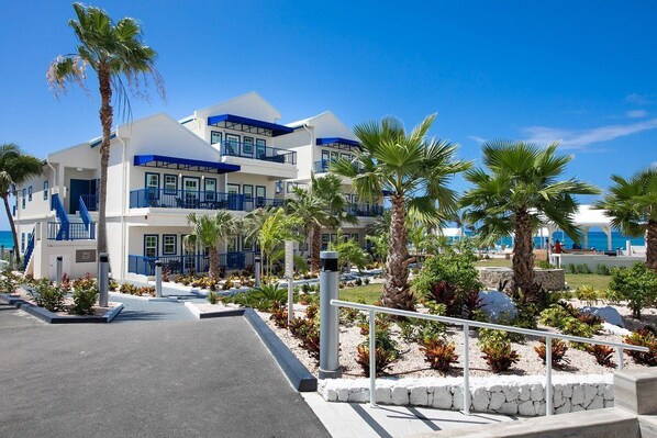 A multi-story hotel with balconies, palm trees, and a clear view of the ocean.