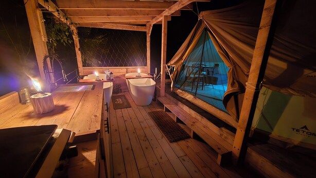 Eine Holzterrasse mit Tisch und Stühlen, einem Whirlpool und einem Zelttbereich mit Blick auf den Nachthimmel.