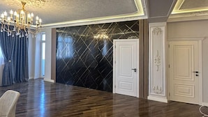 Una habitación amplia con suelo de madera oscura, un candelabro y un gran ventanal con cortinas.