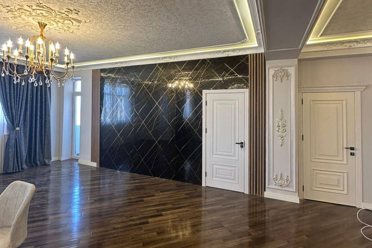 Une pièce spacieuse dotée d’un parquet en bois foncé, d’un lustre et d’une grande fenêtre agrémentée de rideaux.
