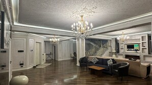 Amplia sala de estar con techo alto, candelabros ornamentales, chimenea y un conjunto de sofás modernos.