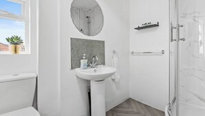Ein Badezimmer mit Toilette, Waschbecken, Spiegel, Dusche und einem Boden mit Fischgrätmuster.