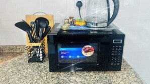 Una cucina con un forno a microonde che mostra uno schermo digitale, un bollitore e diversi alimenti sul bancone.