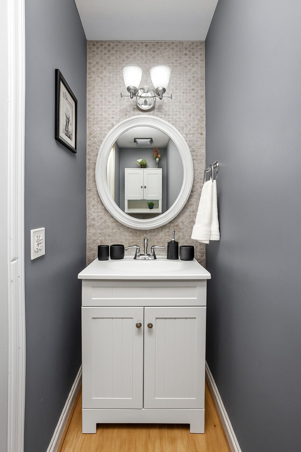 A bathroom with a white vanity, a round mirror, and a wall-mounted light fixture.