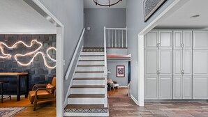 Un escalier menant à un deuxième étage, un coin repas avec une table et des chaises, et une cuisine équipée d’armoires.
