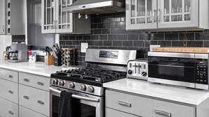 Une cuisine moderne dotée d’appareils électroménagers en acier inoxydable, de meubles de rangement gris et d’un dosseret de crédence en carreaux noirs.