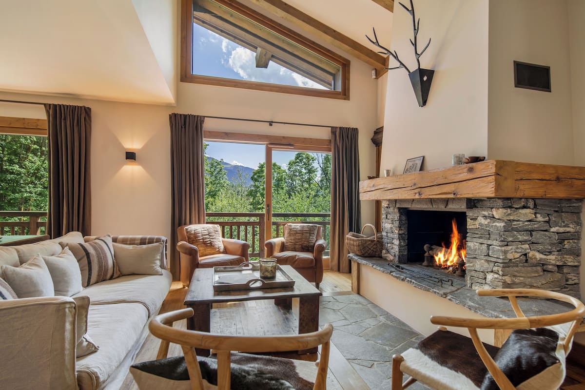 A cozy living room with a stone fireplace, comfortable seating, and a scenic view through large windows.