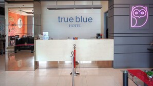 Hotellin vastaanottoalue, jossa on näkyvillä kyltti, jossa lukee »true blue», neonvaloin toteutettu pöllölogo ja vastaanottotiski.