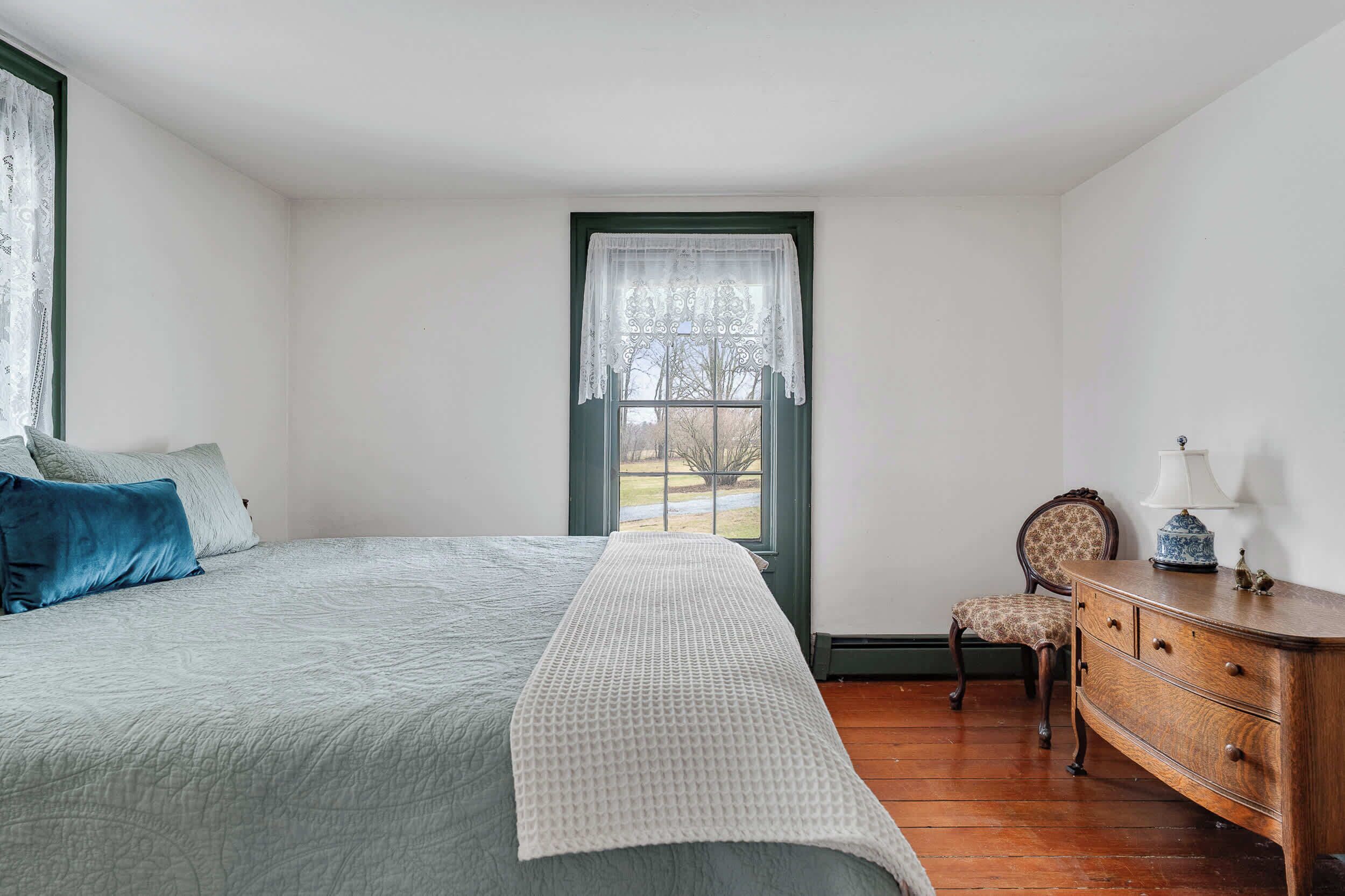 Un dormitorio con cama, una silla, un tocador y una ventana.