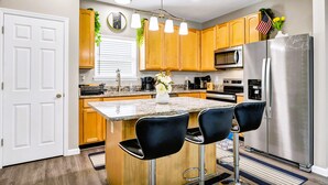 Una cocina moderna con armarios de madera, un refrigerador de acero inoxidable, una encimera de granito y dos taburetes negros.