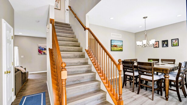 Una escalera con barandillas de madera y un suelo de alfombra azul que conduce a un comedor con una mesa y sillas de madera.