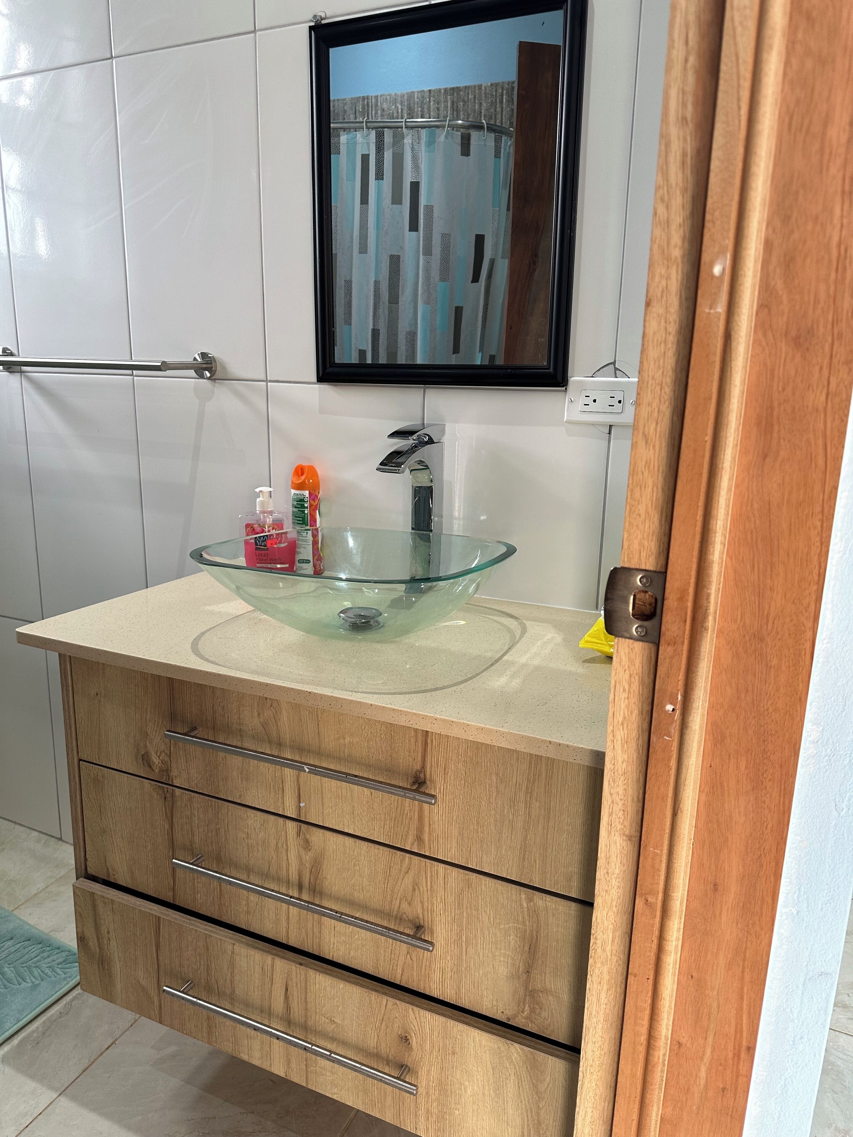 A bathroom with a glass bowl sink, wooden cabinets, a mirror, and a towel rack.