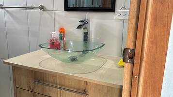 A bathroom with a glass bowl sink, wooden cabinets, a mirror, and a towel rack.
