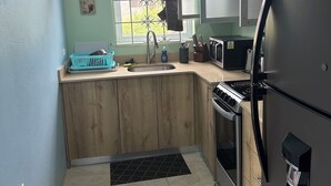 A compact kitchen with a refrigerator, stove, sink, and a window with decorative curtains. - Private Oasis - Portland’s Coastal Gated Hideaway (Fair Prospect)