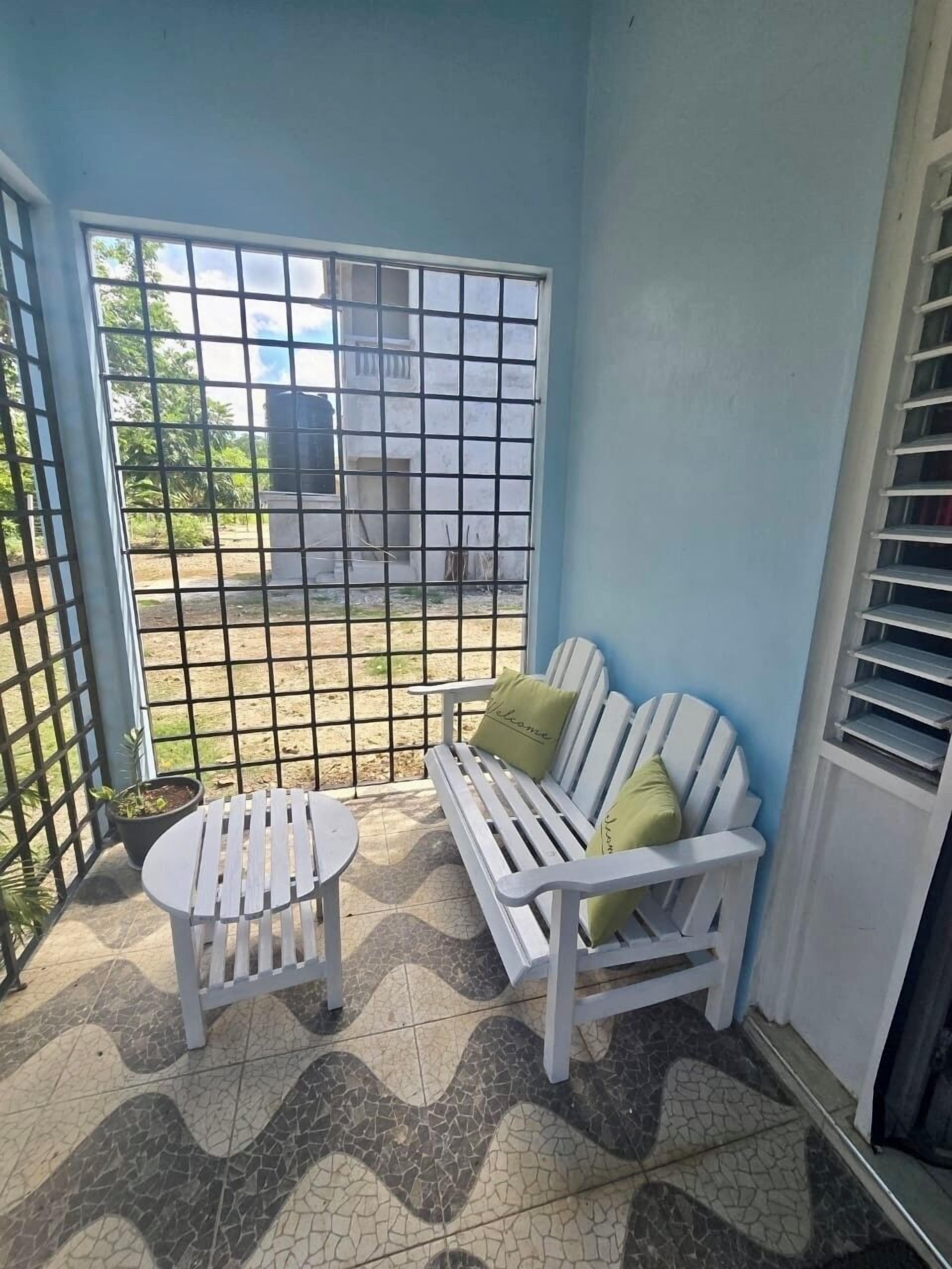 A small balcony with a white sofa and a round table, tiled flooring, and a metal gate.