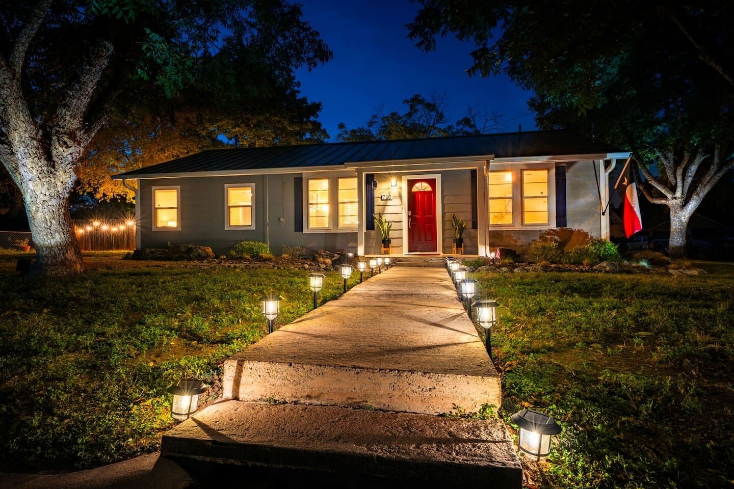 A two-story house with a red door, a front porch, and a pathway lined with lights leading to the entrance.