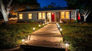 Una casa de dos pisos con puerta roja, un porche y un sendero iluminado que conduce a la entrada.