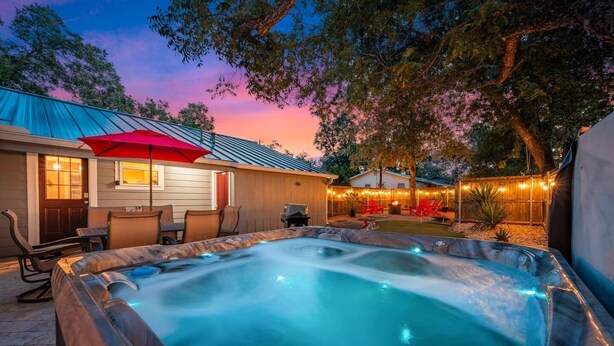Un jacuzzi con cubierta de madera y un patio con sillas y una sombrilla roja.