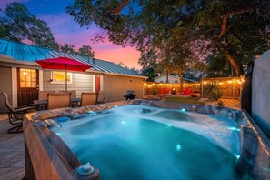 A hot tub with a wooden deck and a patio area with chairs and a red umbrella. - Close to Main St • Wineries w/Hot Tub & Fire Pit (Fredericksburg)