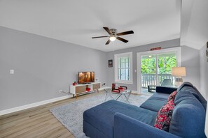A modern living room with a blue sofa, a ceiling fan, a TV, and a view of the outdoors.