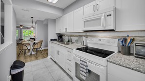 Une cuisine moderne avec des meubles blancs, un four à micro-ondes, une cuisinière et un coin repas comprenant des chaises et une table.