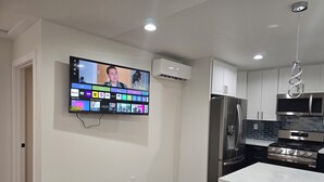 Eine moderne Küche mit Flachbildfernseher an der Wand, der verschiedene Sender zeigt, sowie einem Edelstahl-Kühlschrank, einer Mikrowelle und einem Gasherd.