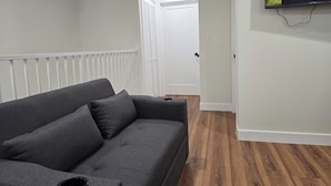 Ein modernes Wohnzimmer mit grauem Sofa, Holzboden und einem Wandfernseher.