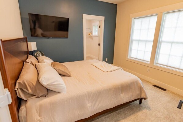 A bedroom with a bed, a TV mounted on the wall, a window, and a door.